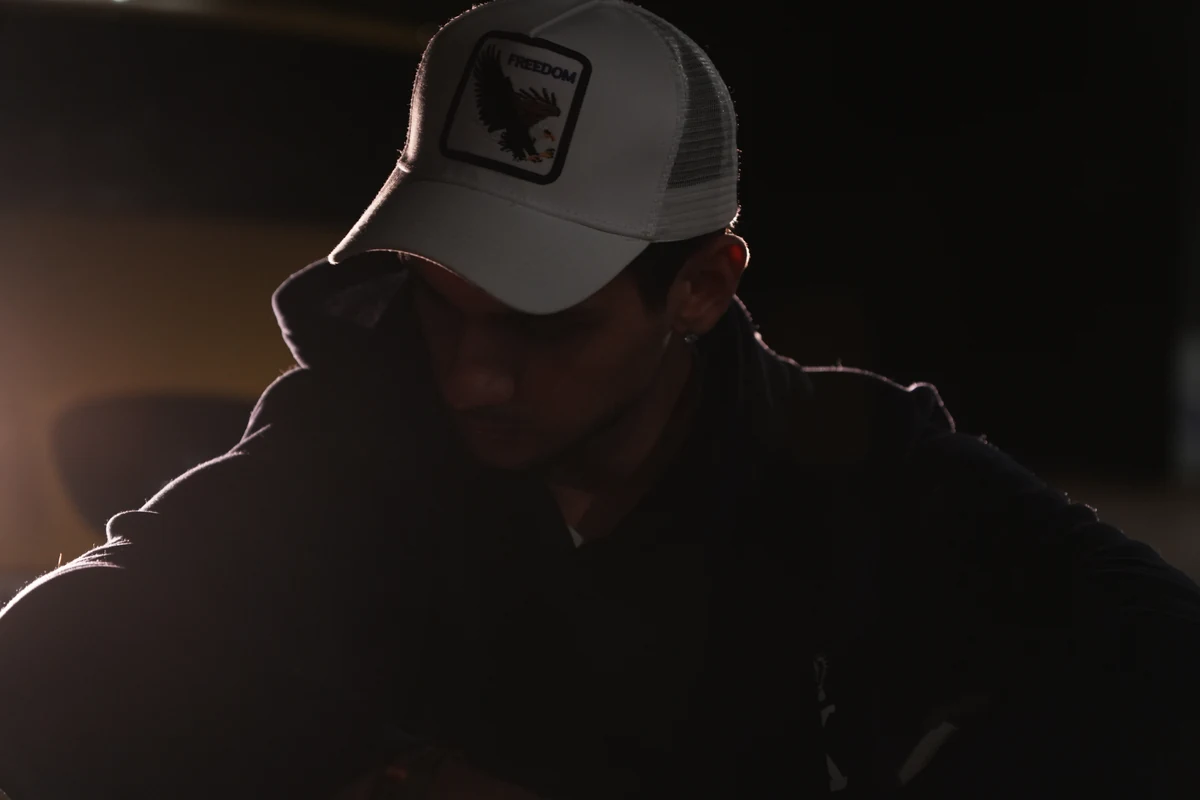 Retrato en penumbra de un chico con gorra blanca mirando hacia abajo, con luz cálida lateral